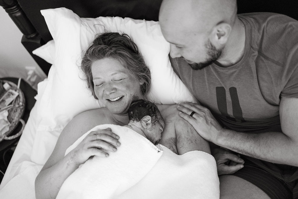 A mother holding her newborn after birth while the father smiles next to them